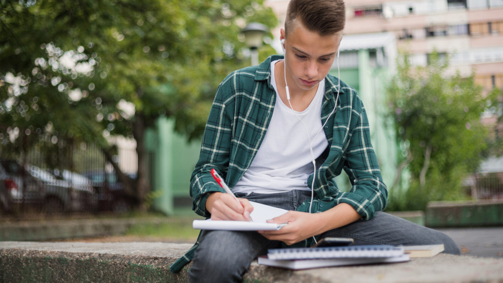 Teenage boy writes in a notebook while listening to music